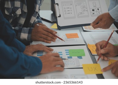 Close up ux developer and ui designer brainstorming about mobile app interface wireframe design on table with customer breif and color code at modern office.Creative digital development agency