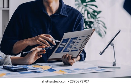Close up ux developer and ui designer brainstorming about mobile app interface wireframe design on table with customer breif and color code at modern office.Creative digital development agency