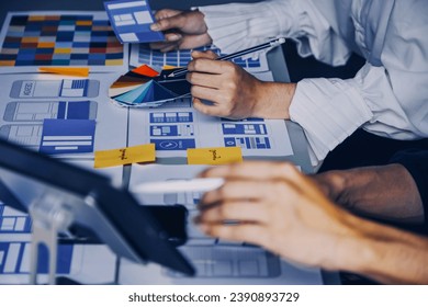 Close up ux developer and ui designer brainstorming about mobile app interface wireframe design on table with customer breif and color code at modern office.Creative digital development agency