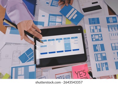Close up ux developer and ui designer brainstorming about mobile app interface wireframe design on table with customer breif and color code at modern office.Creative digital development agency.