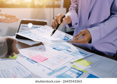 Close up ux developer and ui designer brainstorming about mobile app interface wireframe design on table with customer breif and color code at modern office.Creative digital development agency.