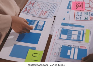 Close up ux developer and ui designer brainstorming about mobile app interface wireframe design on table with customer breif and color code at modern office.Creative digital development agency.