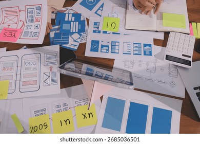 Close up ux developer and ui designer brainstorming about mobile app interface wireframe design on table with customer breif and color code at modern office.Creative digital development agency.