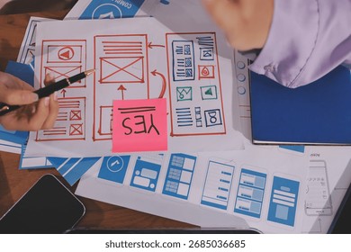 Close up ux developer and ui designer brainstorming about mobile app interface wireframe design on table with customer breif and color code at modern office.Creative digital development agency.