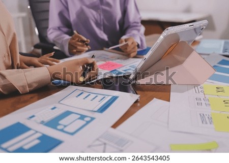 Close up ux developer and ui designer brainstorming about mobile app interface wireframe design on table with customer breif and color code at modern office.Creative digital development agency.