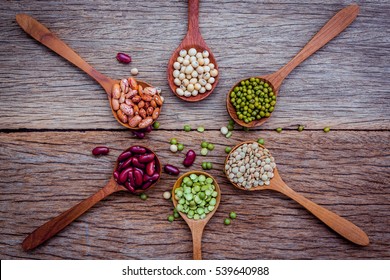 Close up  of various beans in wooden spoons setup on shabby wooden background.