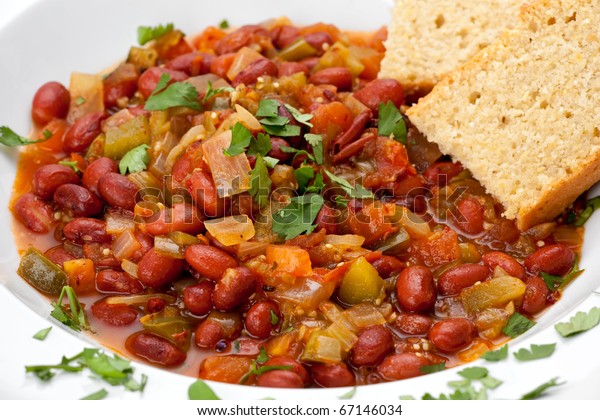 Close up of vegetarian chili with beans, and\
cornbread in a white\
bowl.