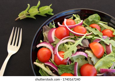 Close Up Vegetarian Salad Bowl With Fork And Blur Mint Leave Beside The Bowl. Photo Isolate On Black Top View 