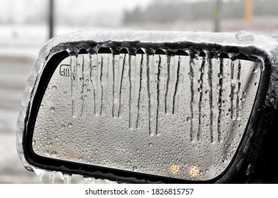 A close up of a vehicles heated side mirror with icicles