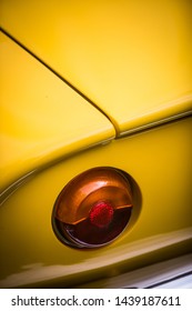 Close up vertical image of the red tail light of a yellow classical vintage car.