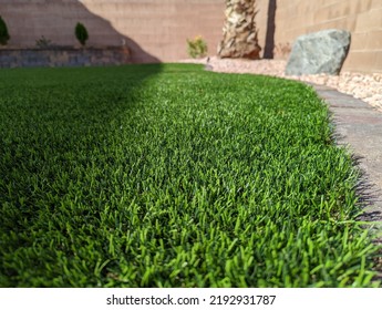 Close Up Of Vibrant Green Artificial Grass Turf In Residential Las Vegas Backyard With Water-efficient Desert Landscaping In The Background.