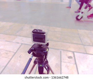 Close up view of an action camera on a tripod  shooting on a pedestrian street. On purpose blurry background with people on the right.