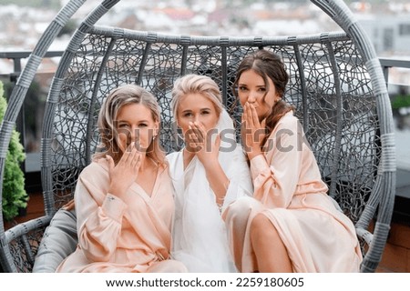 Close view of adorable women with stylish hairdo,  sitting together on swing chair on terrace, sending air kiss while posing at camera