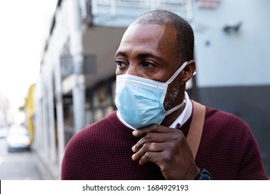 Close Up View Of An African American Man Wearing Red Pullover, Out And About In The City Streets During The Day, Putting On A Face Mask Against Air Pollution And Covid19 Coronavirus.