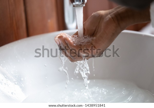 Close up view african man hand gathering clear\
water pouring from faucet into the human palm, concept of personal\
hygiene and morning routine, global climate warming and worldwide\
water crisis problem