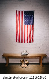 close up view of american flag hanging on white brick wall and arranged military uniform on wooden bench