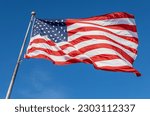 Close up view of an American flag waving on a flagpole, with blue sky background