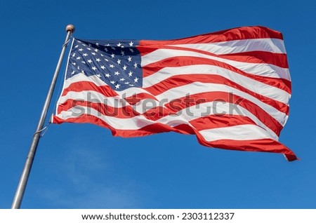 Close up view of an American flag waving on a flagpole, with blue sky background
