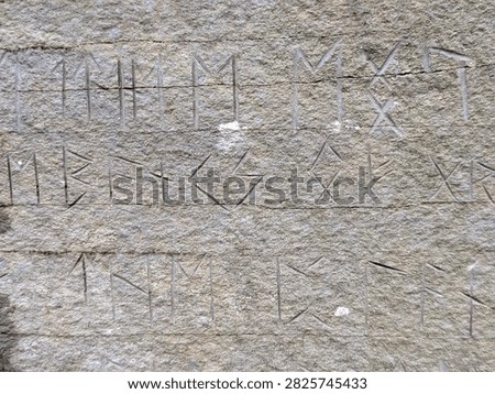 Close up view of ancient Viking runic alphabet symbols deeply engraved into a textured gray stone surface.