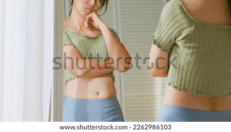 close up view - asian woman standing in front of mirror and dissatisfied about her body shape