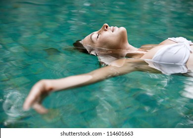 Close up view of an attractive young woman floating on a spa's swimming pool, smiling.