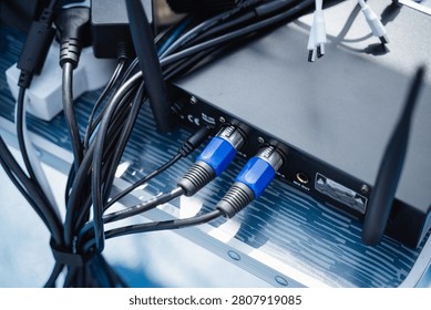 Close view of audio interface rear panel with blue XLR connector cables, tangled black wiring, and metal equipment case surface, lit by cool daylight for studio and broadcast use, with audio