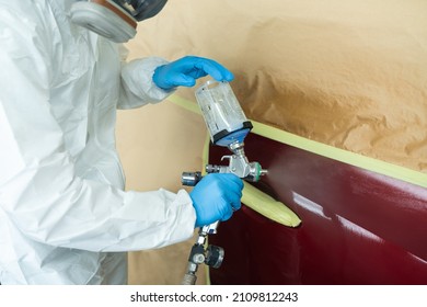 Close Up View Of Auto Painter In A Protective Suit And Mask Sprays A Degreaser Or Other Cleaner On A Car Door Using A Spray Gun. Preparation Of Vehicle Body Elements For Local Repair