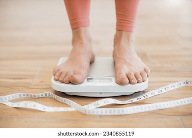 Close up view of barefoot human legs in tight-fitting terracotta pants standing on mechanical scales on wooden floor. Athletic person going through weight control check after body tape measurement. - Powered by Shutterstock