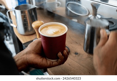 Close up view of barista with hot streaming milk pouring a delicious golden flat white coffee in disposable cup at local coffee shop - Powered by Shutterstock