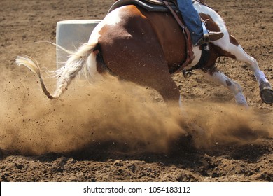 A close up view of a barrel racing horse kicking up dirt and dust sliding around the barrel.