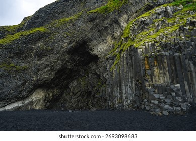Close view of basalt columns on Reynisfjara Beach in Vik, Iceland. Moss traces, fractured lava, and a shadowed cavern show volcanic textures in soft overcast light.