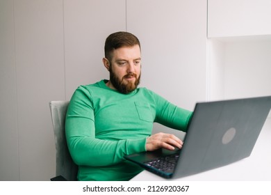 Close up view of bearded middle aged man in green t-shirt using laptop computer on the white wall background typing text. Male is working. Businessman, Teacher. Mock up copy space. - Powered by Shutterstock