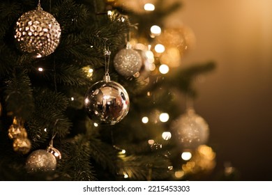 Close up view of beautiful fir branches with shiny golden bauble or ball, xmas ornaments and lights, Christmas holidays background. copy space. Decoration on christmas tree. Festive new 2023 year.