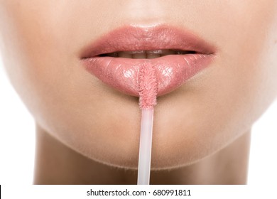 close up view of beautiful woman applying pink lipgloss on lips, isolated on white