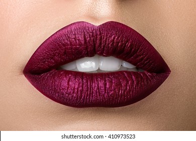 Close up view of beautiful woman lips with purple matt lipstick. Open mouth with white teeth. Cosmetology, drugstore or fashion makeup concept. Beauty studio shot. Passionate kiss