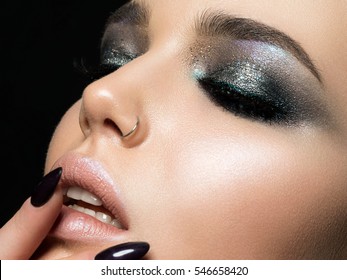 Close up view of beautiful woman touching her lips. Perfect skin and evening makeup. Macro studio shot. Sensuality, passion, cosmetology, lip care, plastic surgery or injection concept.