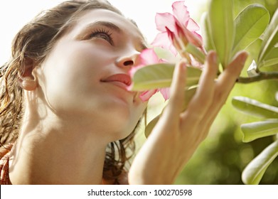 Close Up View Of A Beautiful Young Woman Holding A Flower Close To Her Nose And Smelling The Perfume, Smiling.