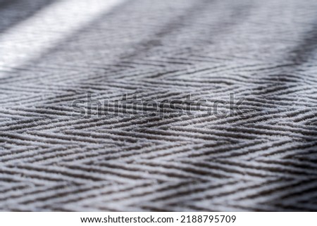 A close up view of a bedspread with a clearly visible fabric texture and weave. The sun's rays through the window fall on the bedspread. Zigzag or chevron pattern.