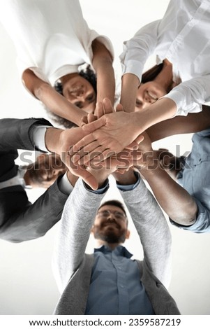 Close up view from below of excited multiracial businesspeople stack hands in pile motivated for shared victory, happy multiethnic colleagues engaged in teambuilding activity, show team unity
