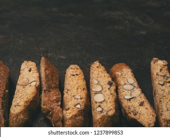 Close View Of Biscotti - Traditional Italian Almond Dessert On Dark Background. Cookies Arranged On The Bottom Of Third Of The Frame With Copy Space. Top View, Selective Focus, Horizontal Composition