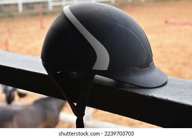 Close up view of  black Equestrian helmet with blurred horse farm view. Isolated Horse riding hat on the railing in the horse farm. - Powered by Shutterstock