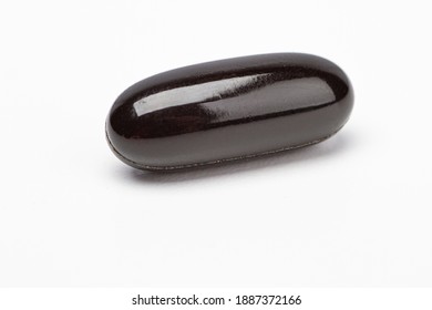 Close up view of a black omega supplement pill against a white background