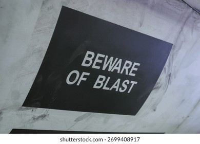Close view of a black and white warning label reading beware of blast on metallic fuselage surface of a multirole fighter jet