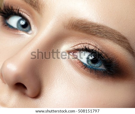 Close up view of blue woman eye with beautiful golden shades and black eyeliner makeup. Classic make up. Perfect brows. Studio shot