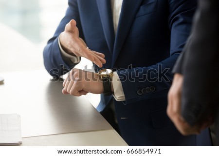 Close up view of businessman wearing suit pointing on hand expensive luxury wristwatch at meeting, showing unpunctual partner he is being late, punctuality management concept, time is money 