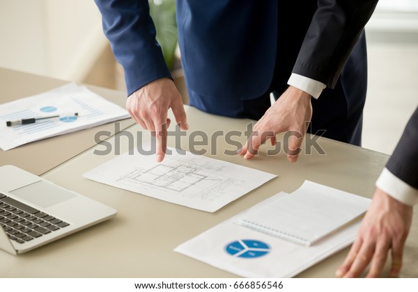 Close up view of businessmen discussing\
building plan, property value estimation, analyzing real estate\
market with infographic statistics, house evaluation, construction\
investment, home appraisal\
