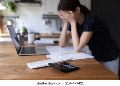 Close up view calculator and bills on table, desperate young woman on background, makes expenses and earnings analysis feels tired and disappointed. Lack of money, overspend, debt, financial troubles - Shutterstock ID 2144499421