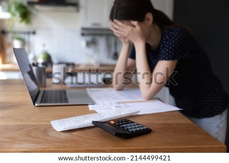 Close up view calculator and bills on table, desperate young woman on background, makes expenses and earnings analysis feels tired and disappointed. Lack of money, overspend, debt, financial troubles