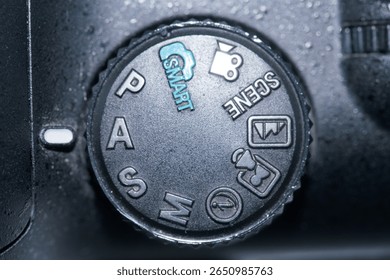 Close up view of a camera mode dial featuring options like Smart, PAS, Scene, and additional settings for capturing images. The dial is designed for easy selection during shooting.
