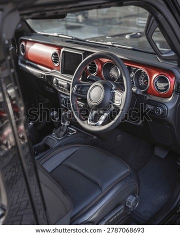 Close up view of a car interior featuring a red accented dashboard and steering wheel with digital gauges.